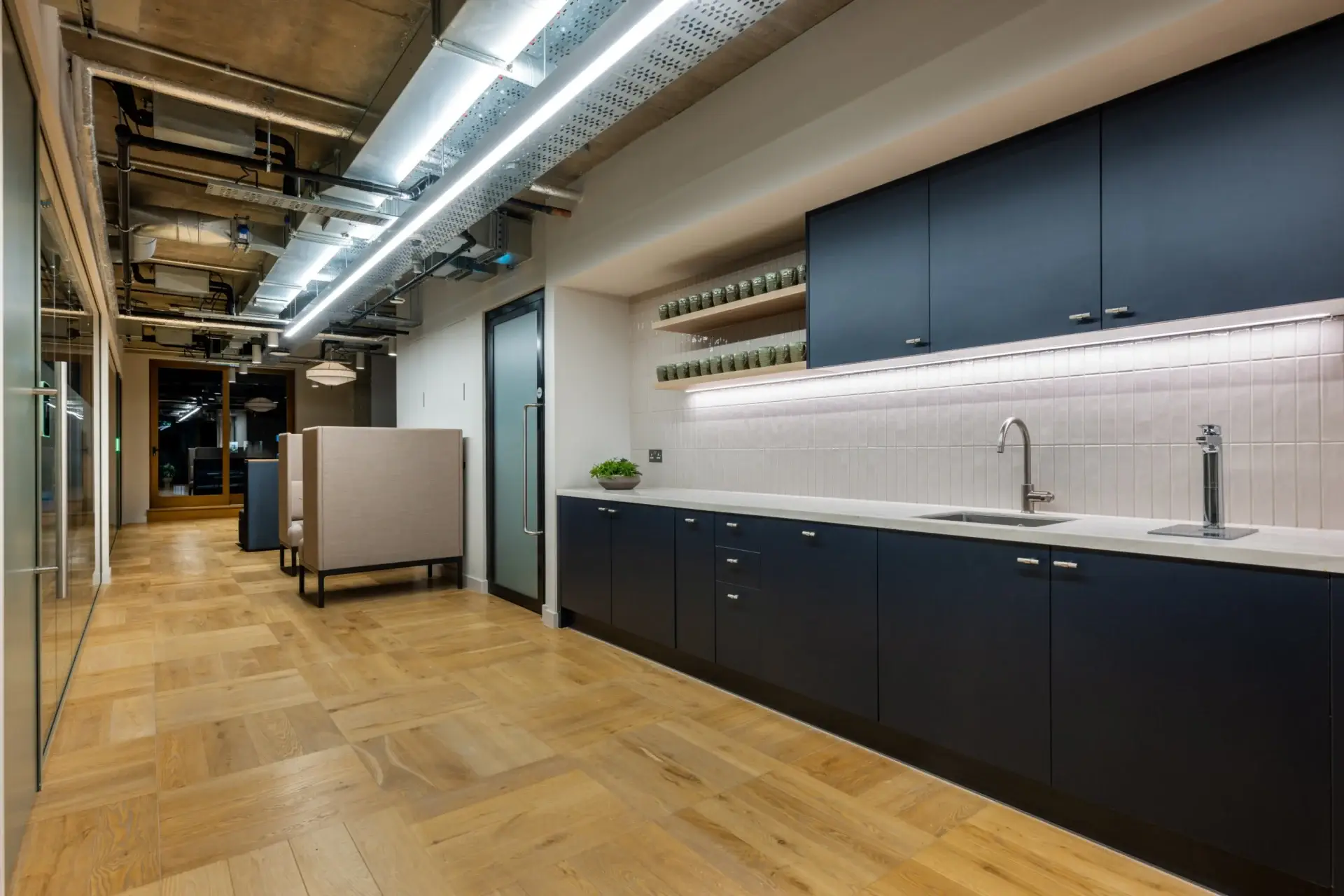 Navy tea point at Equal Experts with a solid surface worktop, oak open shelves and a vertical tiled splashback